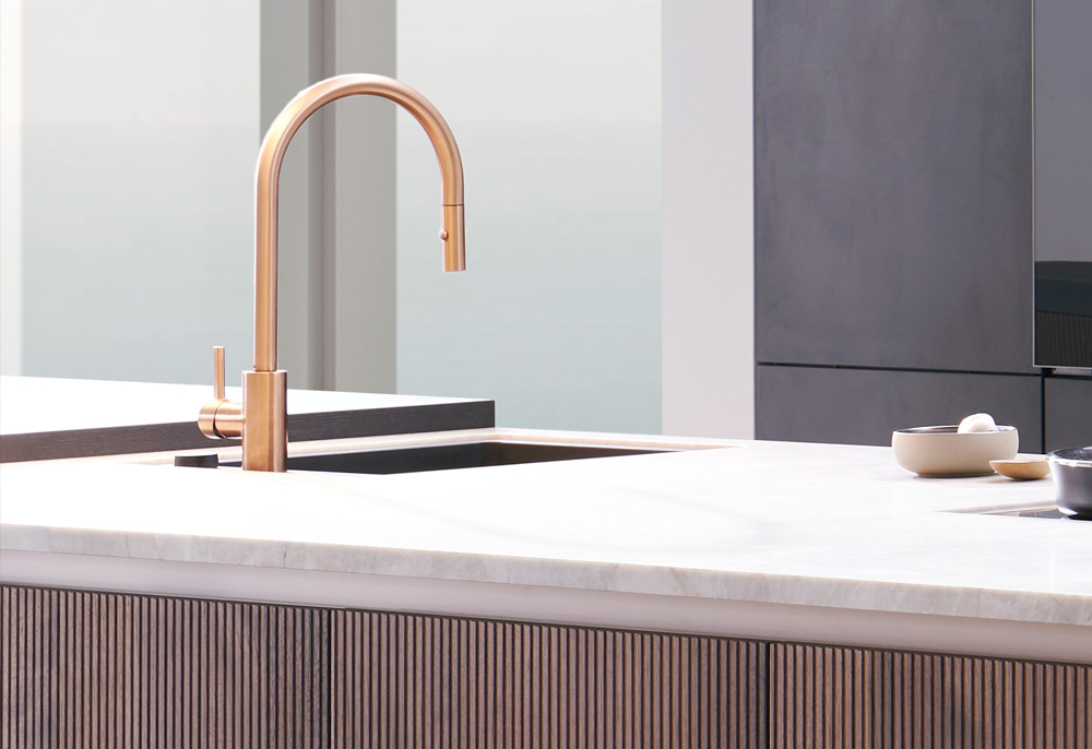 ein goldener Wasserhahn über einem Waschbecken einer Küchenzeile, moderne Optik mit naturstein Oberflächen