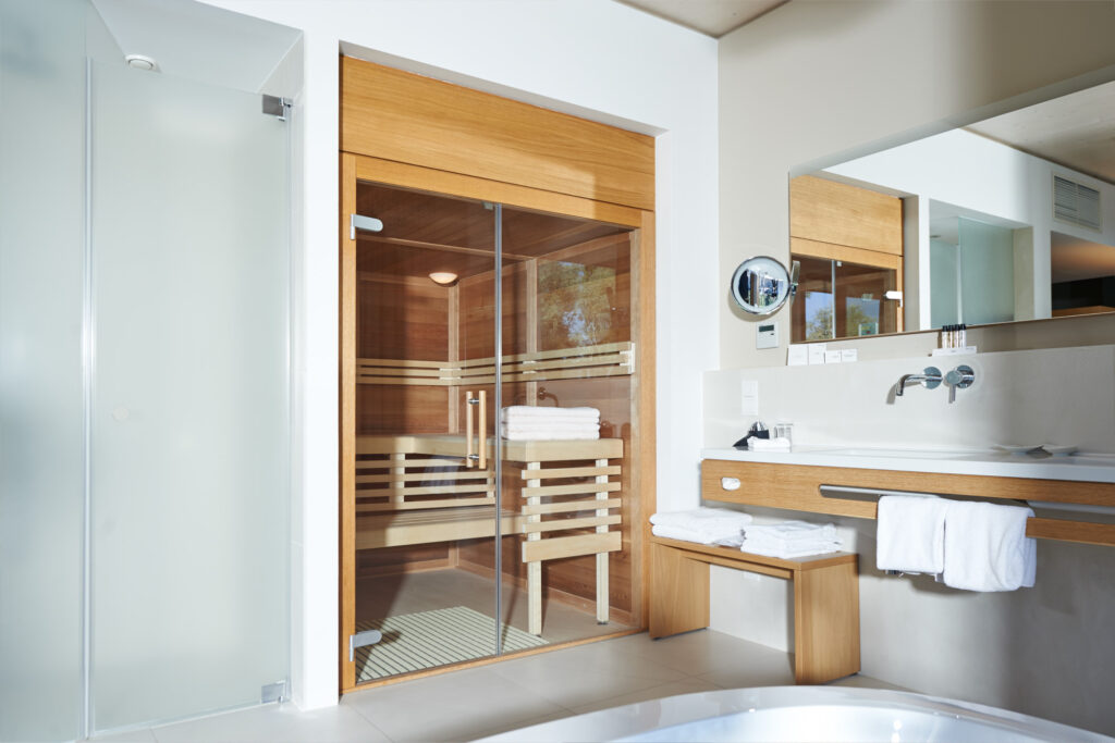 Infrarot Wärmekabine in Hotelzimmer, daneben Waschbecken mit Holzoptik und Spiegel